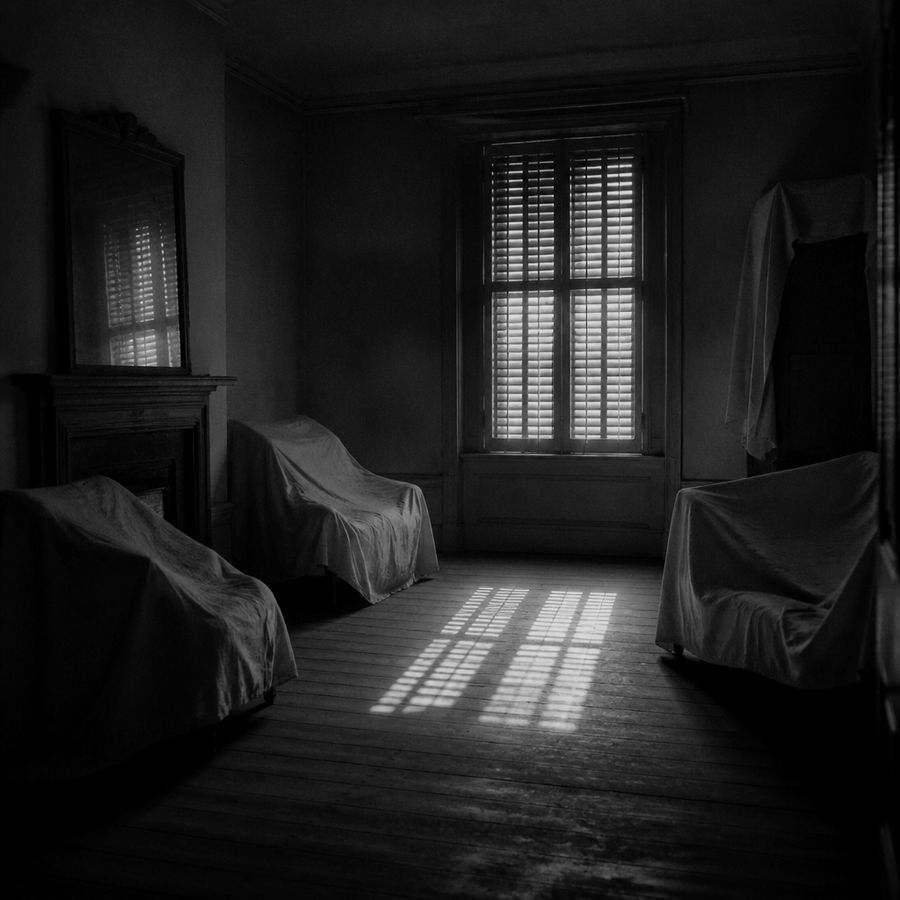 Empty room with furniture under dust sheets, light through a shuttered window